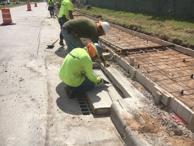 Crew hand-finishing concrete curb and gutter with a drainage inlet