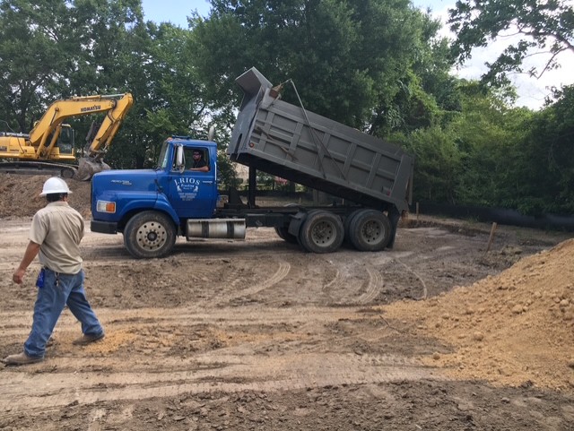 Dump truck unloading fill dirt with an excavator working in the background